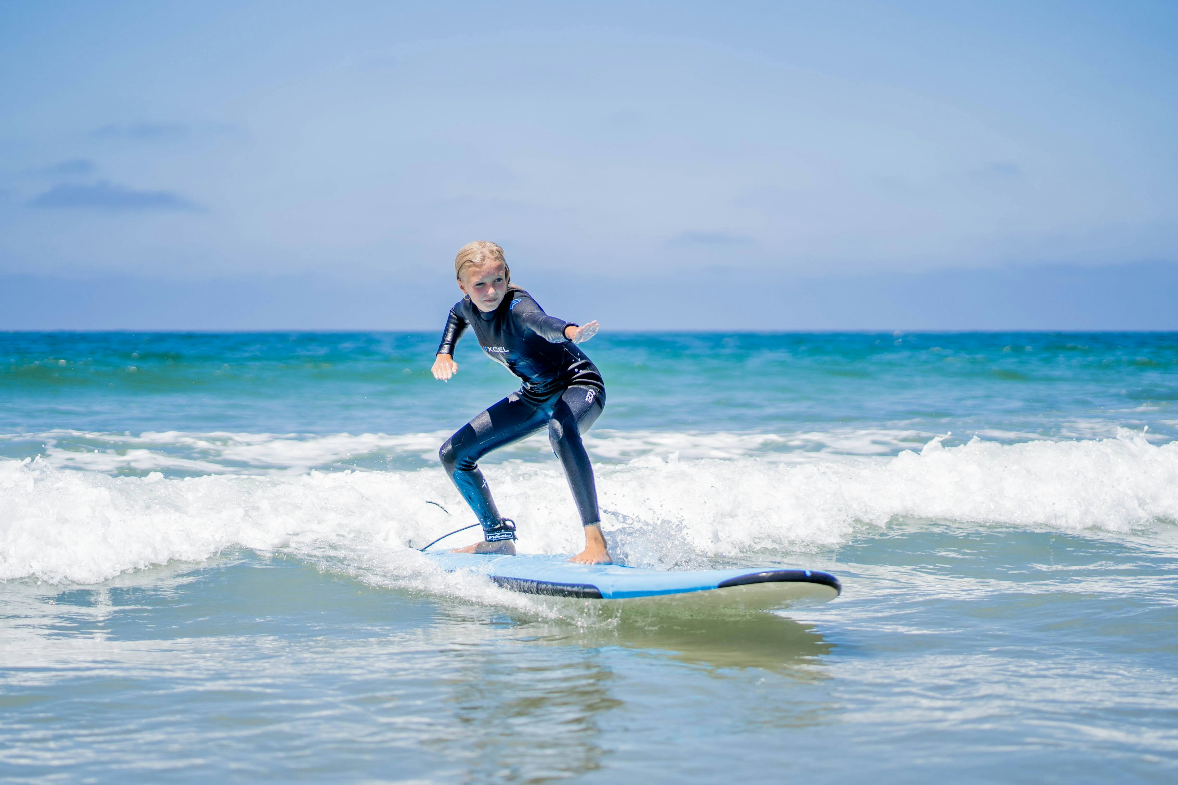 A young student leading with her arms in the ocean on her surf board.