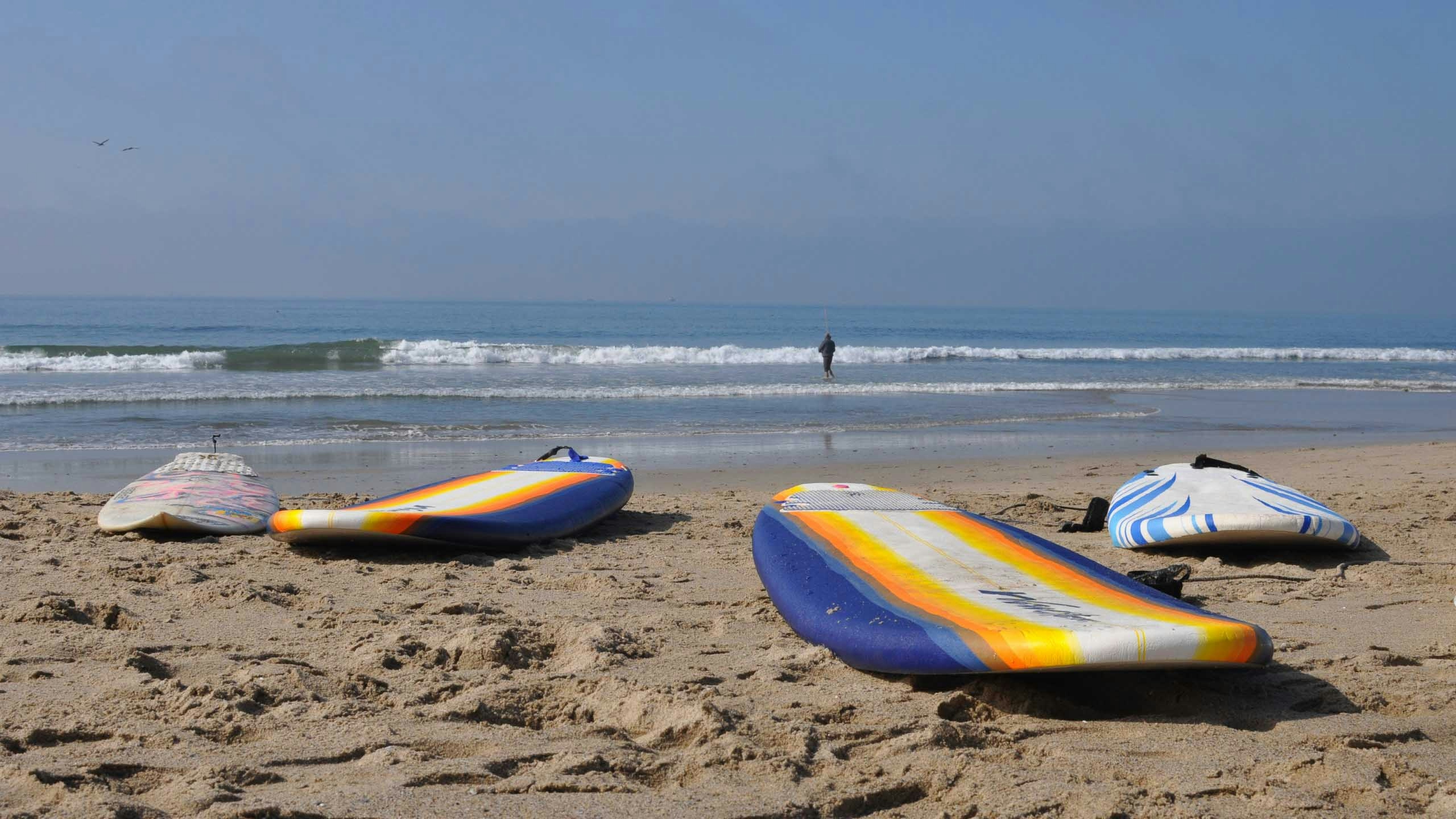 Surfboards on the sand of Will Rogers beach with small waves in the ocean.