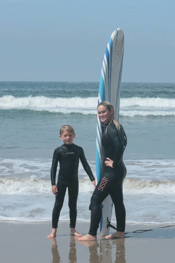 Young surfers standing with a surfboard at the shoreline.
